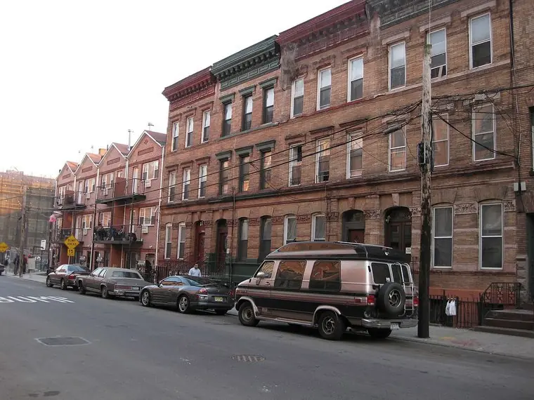 Row of brick apartment buildings with bracketed cornices on a Bronx street