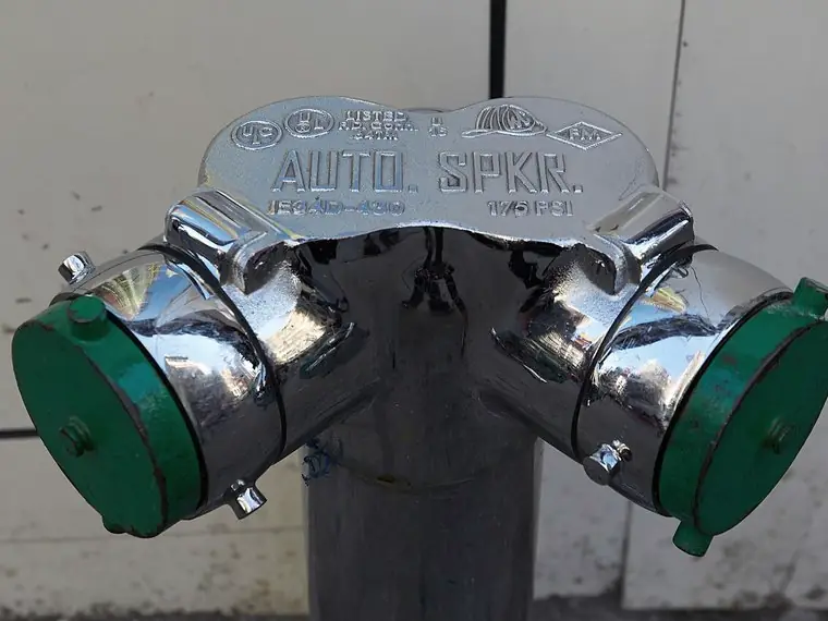 Chrome fire department connection standpipe with green caps on a New York building